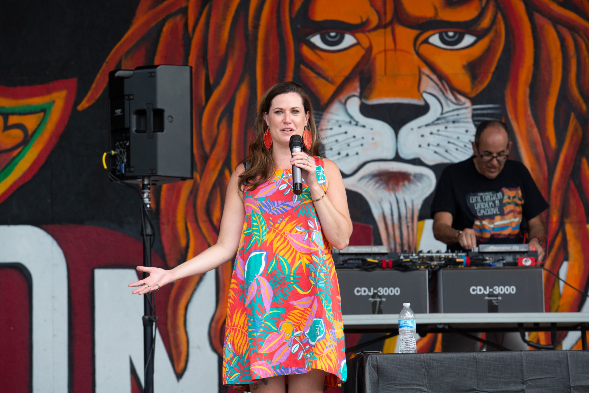 Speaker on stage at an outdoor community event with a painted tiger backdrop